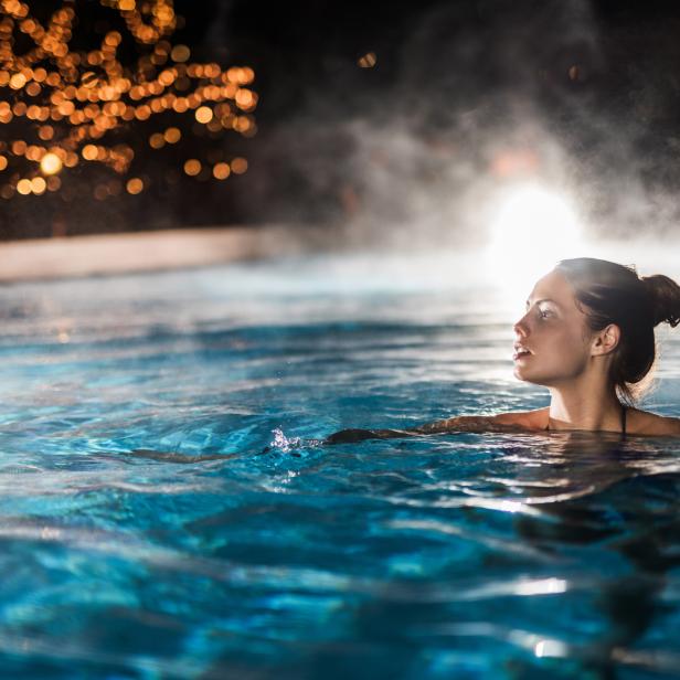 Eine Frau entspannt in einem Schwimmbad mit warmem, dampfendem Wasser.