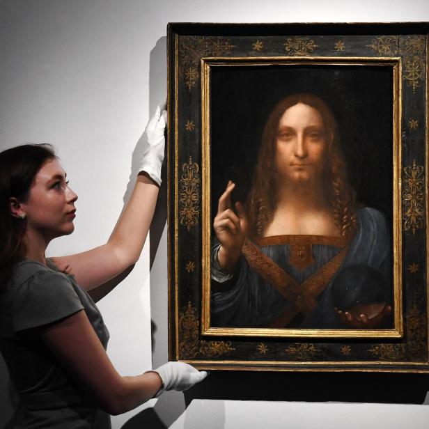 Eine Frau mit weißen Handschuhen hantiert mit dem Gemälde „Salvator Mundi“ von Leonardo da Vinci.