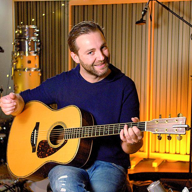 Ein Mann sitzt in einem Tonstudio und spielt Gitarre.