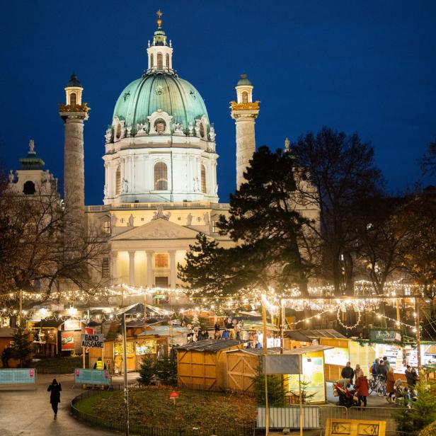 Die Karlskirche in Wien mit einem Weihnachtsmarkt im Vordergrund.