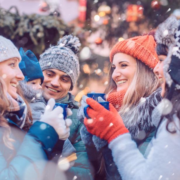 Eine Gruppe von Freunden genießt gemeinsam Glühwein auf einem Weihnachtsmarkt.