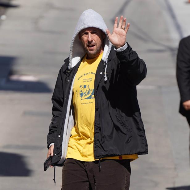 Adam Sandler mit Kapuze winkt in die Kamera.