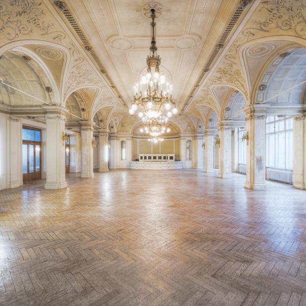 Ein leerer Ballsaal mit Parkettboden und verzierten Deckenleuchtern.