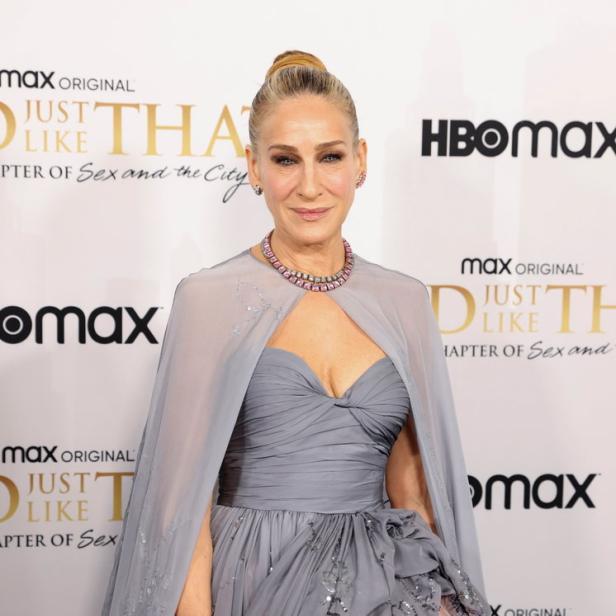 Sarah Jessica Parker in einem grauen Kleid mit rosa Akzenten auf einem roten Teppich.