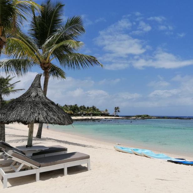 Ein Strand mit Liegestühlen, einem Sonnenschirm und einem türkisfarbenen Meer.