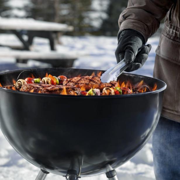 Ein Mann grillt Steaks und Gemüsespieße im Winter.