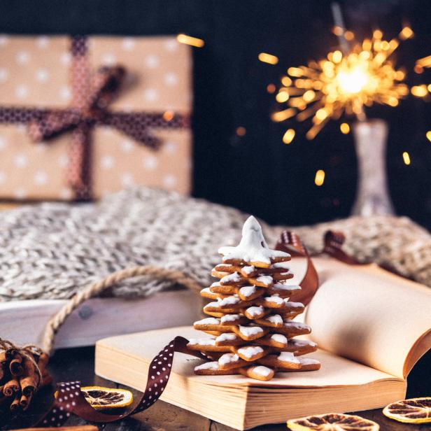 Ein Lebkuchen-Tannenbaum steht auf einem Buch, umgeben von weihnachtlicher Dekoration.