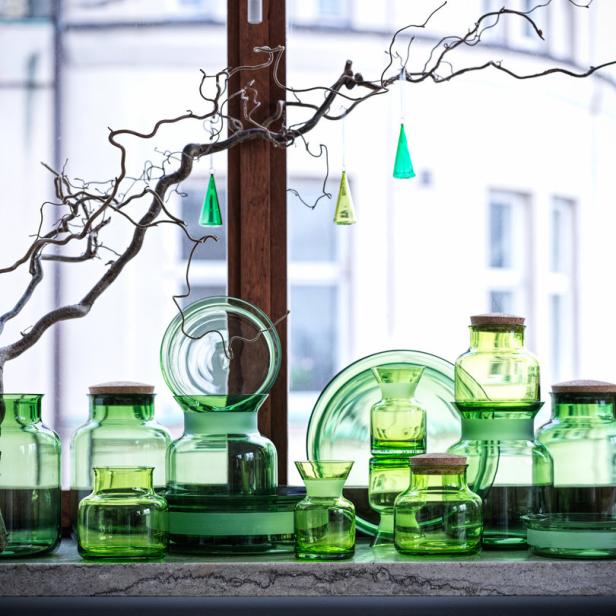 Grüne Glasvasen und Dekorationen stehen auf einem Sims vor einem Fenster.