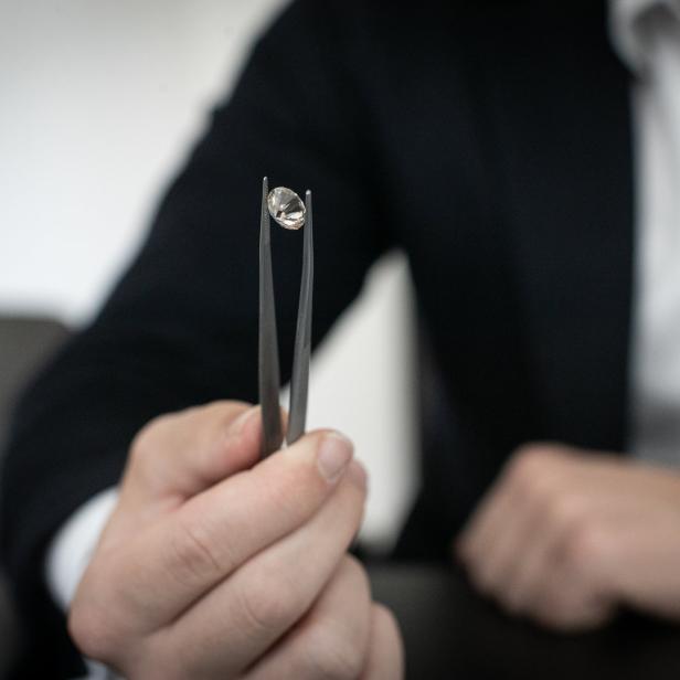 Ein Mann im Anzug hält einen Diamanten mit einer Pinzette.