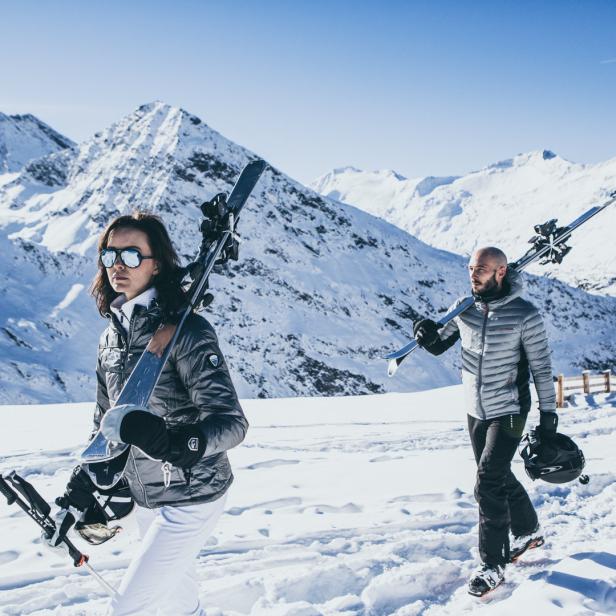 Eine Frau und ein Mann tragen Skier durch eine verschneite Berglandschaft.