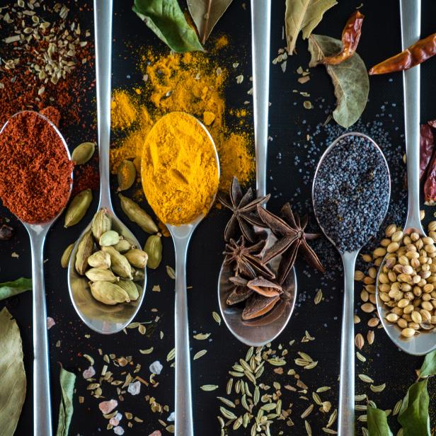 Verschiedene Gewürze wie Curry, Kardamom und Sternanis auf Löffeln präsentiert.