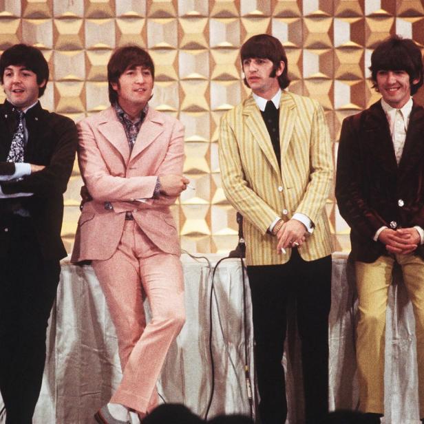 Die Beatles posieren in Anzügen vor einem gemusterten Hintergrund.