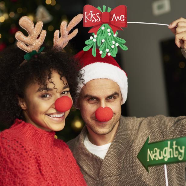 Ein Paar mit roten Nasen und Weihnachtskopfschmuck posiert vor einem Weihnachtsbaum.