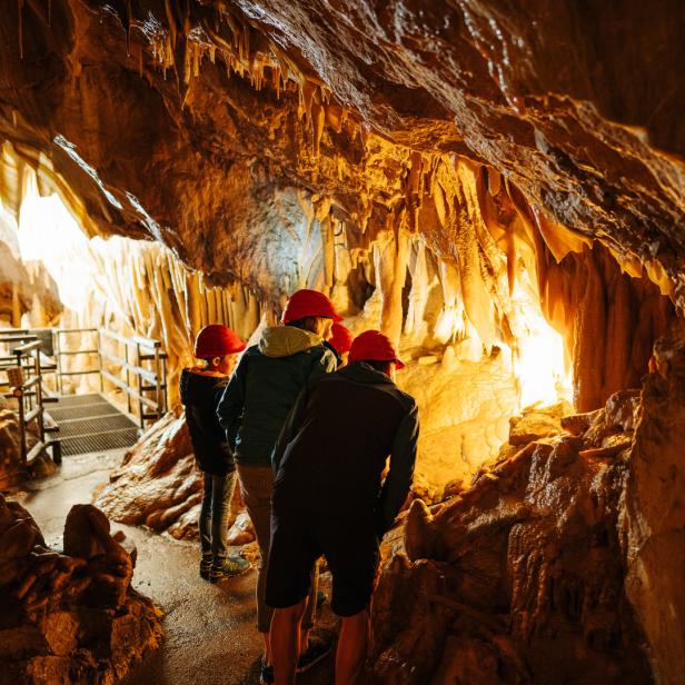 Eine Gruppe von Menschen mit Helmen erkundet eine Höhle mit Stalaktiten.