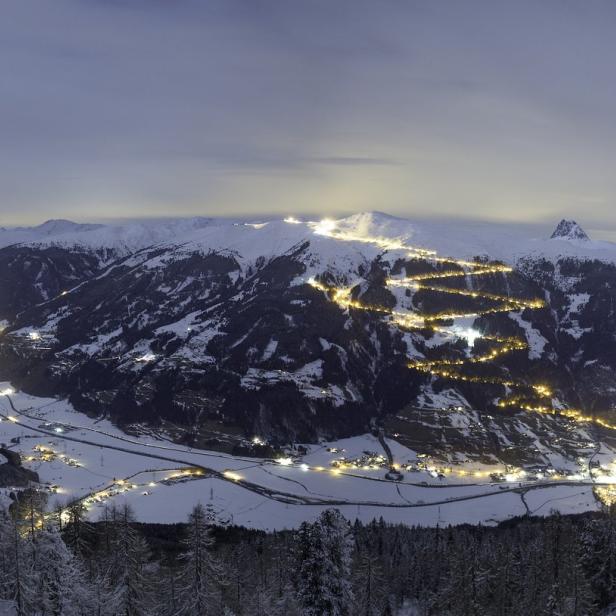 Nachts beleuchtete Skipiste schlängelt sich einen schneebedeckten Berg hinauf.