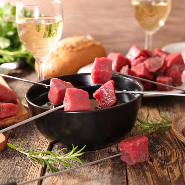 Ein Tisch mit Fondue-Fleisch, Spießen und Weißwein für ein gemütliches Essen.