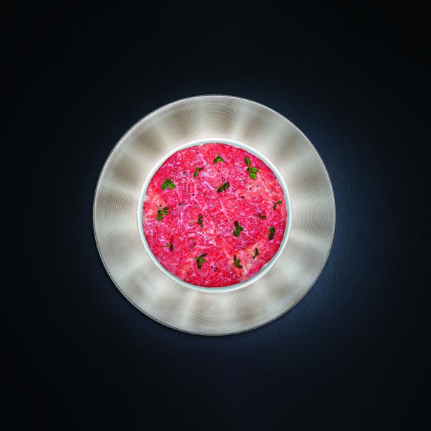 Carpaccio mit Kräutern auf einem Teller vor schwarzem Hintergrund.