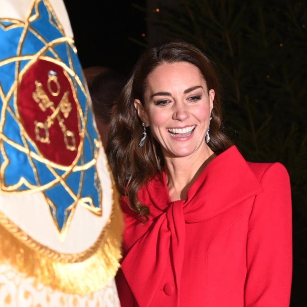 Catherine, Prinzessin von Wales, lächelt neben einer bestickten Fahne.