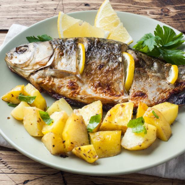 Ein gebratener Fisch mit Zitronenscheiben und Kartoffeln auf einem Teller.