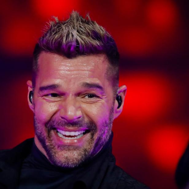 Ricky Martin lächelt vor einem roten Hintergrund.