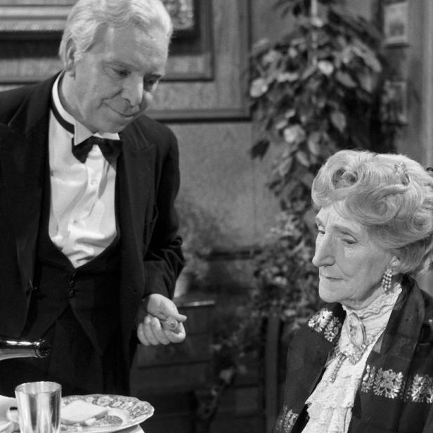 Ein Butler serviert einer älteren Dame ein Getränk.