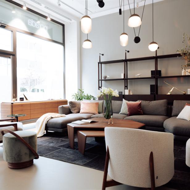 Ein modernes Wohnzimmer mit grauer Couch, Sesseln und Holztischen.