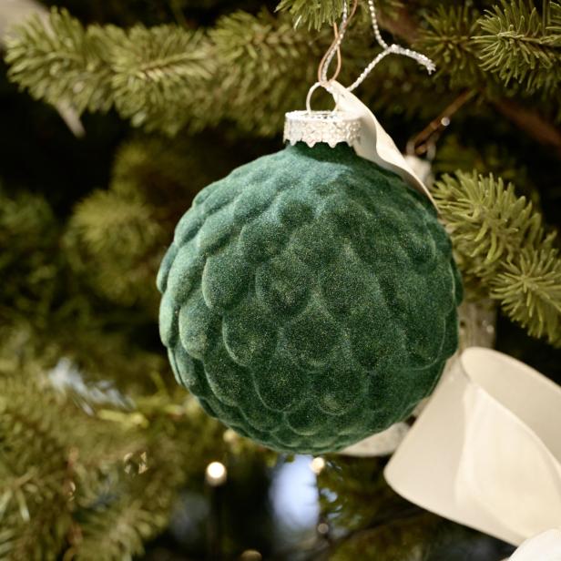 Eine grüne, samtartige Weihnachtskugel hängt an einem Weihnachtsbaum.