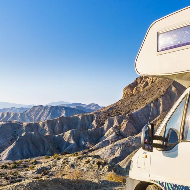 Ein Wohnmobil steht vor einer weiten Wüstenlandschaft unter blauem Himmel.