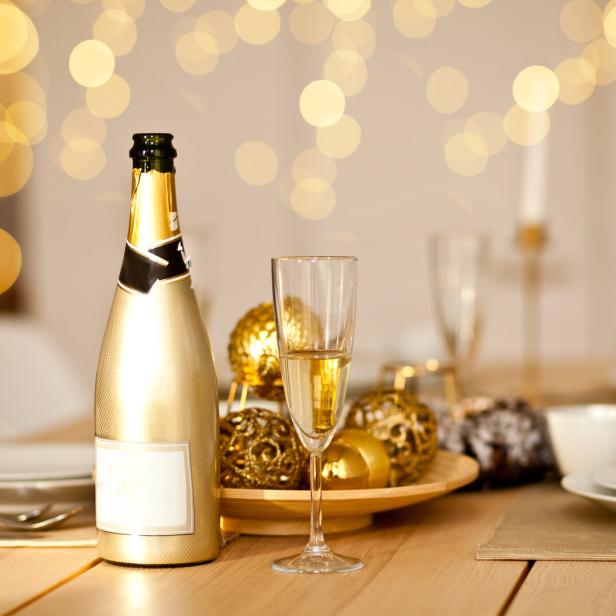 Eine goldene Sektflasche und ein gefülltes Glas stehen auf einem festlich gedeckten Tisch mit goldener Dekoration.