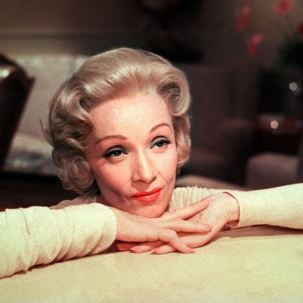 Marlene Dietrich ruht mit verschränkten Händen auf einem Tisch.