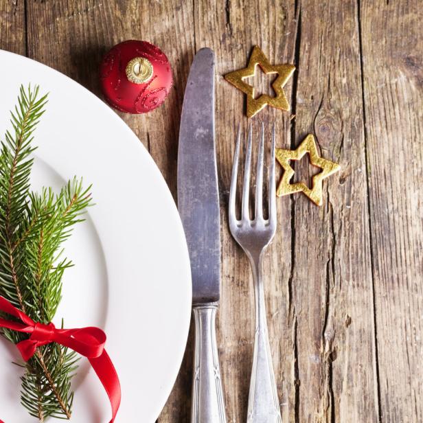 Ein festlicher Weihnachtstisch mit Tannenzweig, roter Kugel und goldenen Sternen.