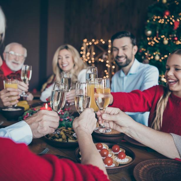 Eine Familie stößt an Weihnachten mit Sekt und Saft an einem festlichen Tisch an.