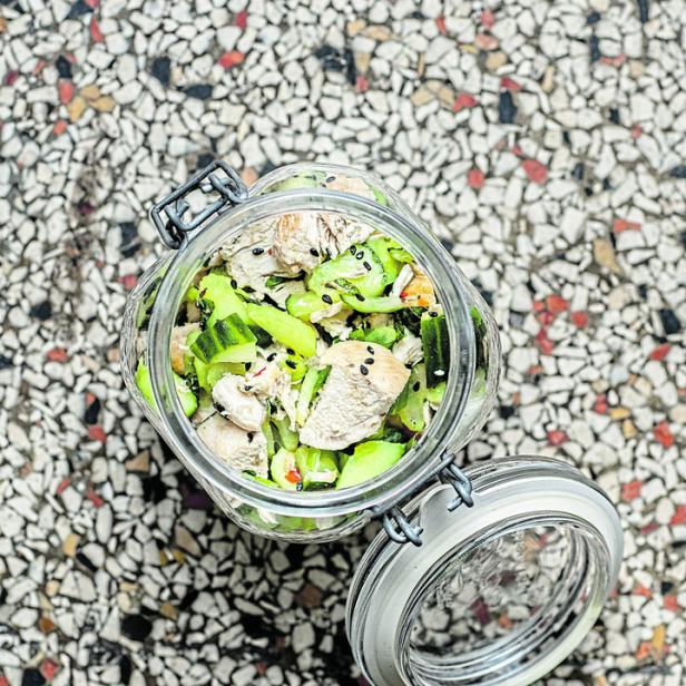 Ein offenes Einmachglas enthält einen Salat mit Hühnchen und Gurken.