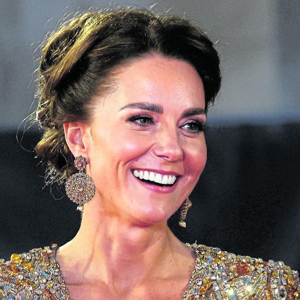 Herzogin Kate lächelt und trägt ein goldenes Kleid und Ohrringe.