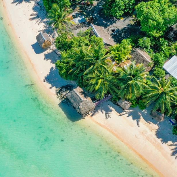 Luftaufnahme eines Strandes in Kiribati mit Palmen und Hütten.
