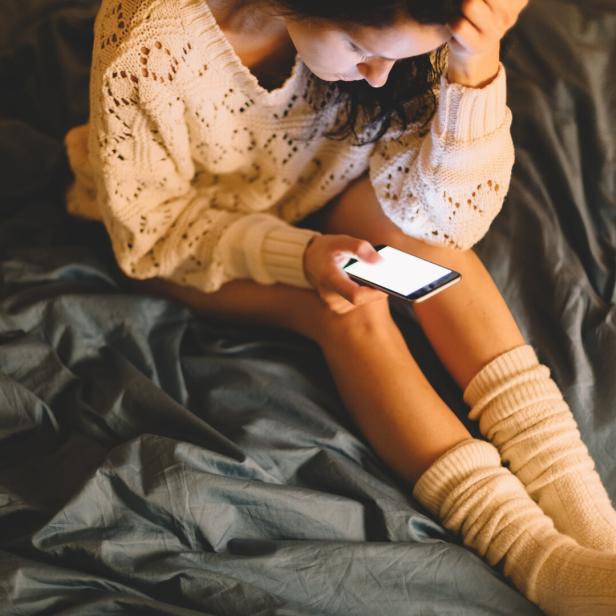 Eine frustrierte Frau sitzt im Bett und schaut auf ihr Handy.