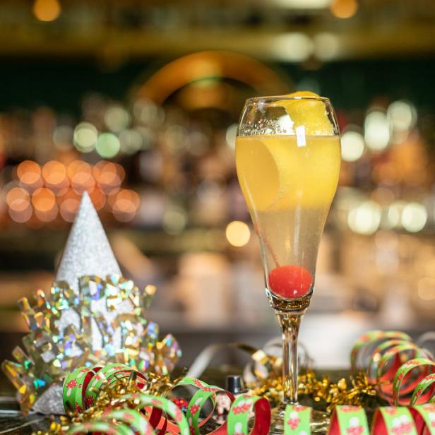 Ein festliches Glas Cocktail mit Kirsche und Zitronenzeste, umgeben von Partyhüten und Luftschlangen.