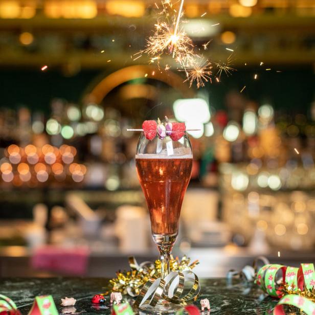 Ein Cocktail mit Himbeeren wird mit einer Wunderkerze serviert, umgeben von festlicher Dekoration.