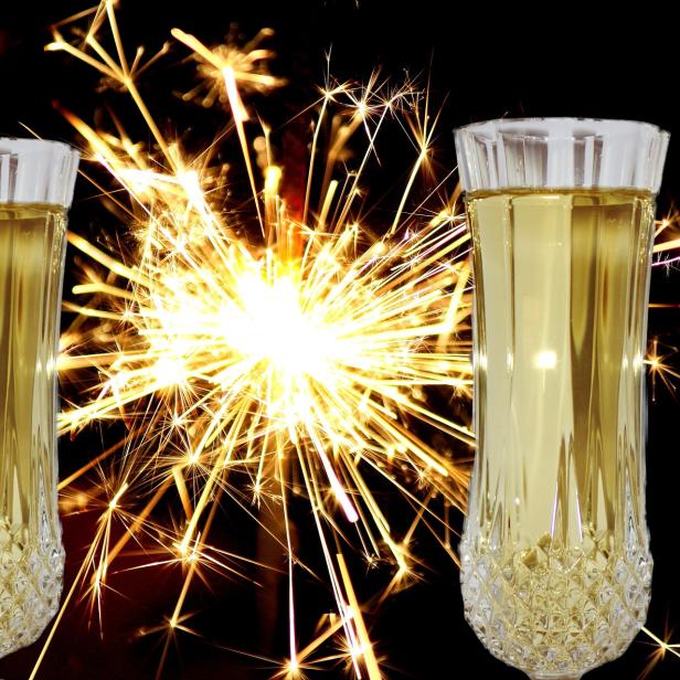 Zwei Sektgläser stehen vor einem hellen Feuerwerk.