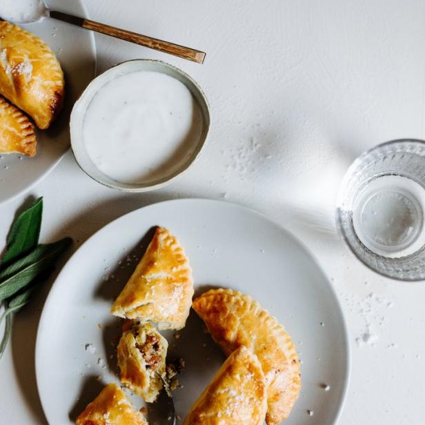 Auf Tellern liegen goldbraune Empanadas, eine davon ist angeschnitten.