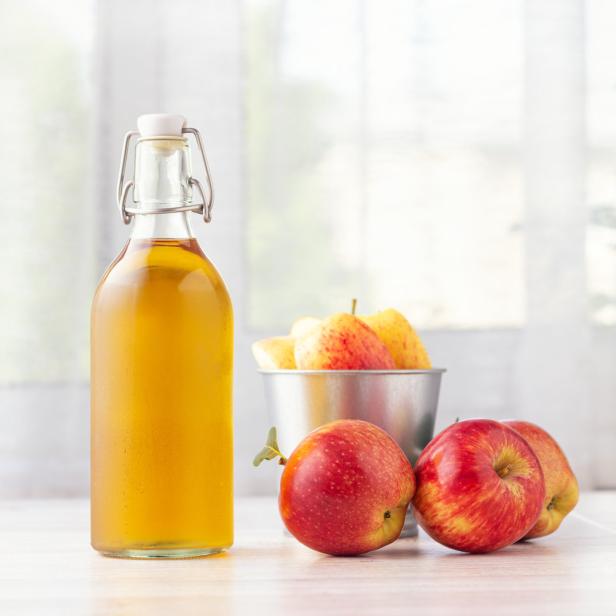 Eine Flasche Apfelessig und rote Äpfel auf einem Tisch.