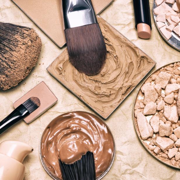 Verschiedene Make-up-Produkte und Pinsel liegen auf einem beigen Hintergrund.