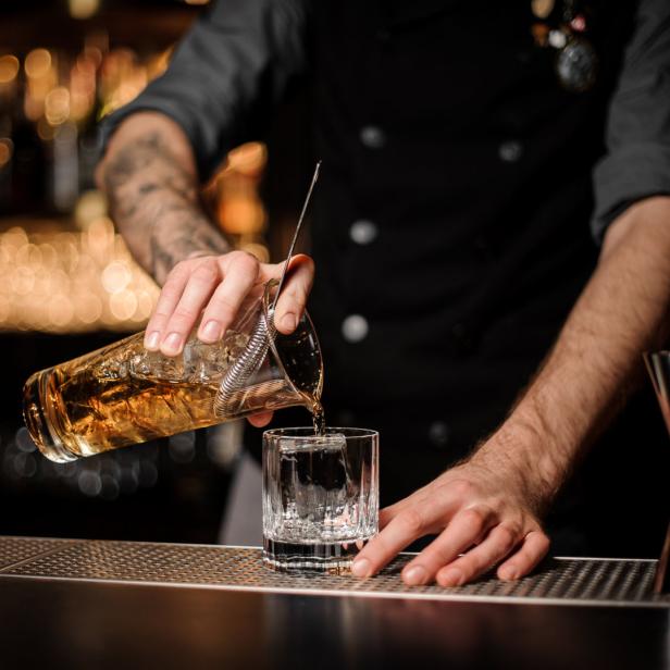 Ein Barkeeper gießt ein Getränk mit Eiswürfeln in ein Glas.