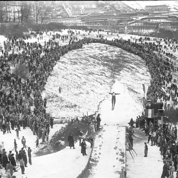Ein Skispringer in der Luft vor einer großen Zuschauermenge an der Skisprungschanze am Himmelhof.