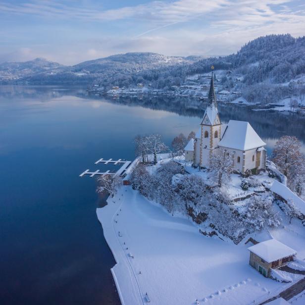 Eine schneebedeckte Kirche am Ufer eines Sees im Winter.
