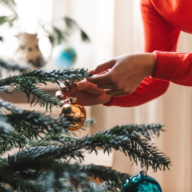 Eine Person schmückt einen Weihnachtsbaum mit goldenen und blauen Kugeln.
