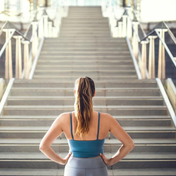 Eine Frau in Sportkleidung steht vor einer langen Treppe.