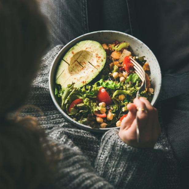 Eine Person isst eine Schüssel Salat mit Avocado, Kichererbsen und Tomaten.