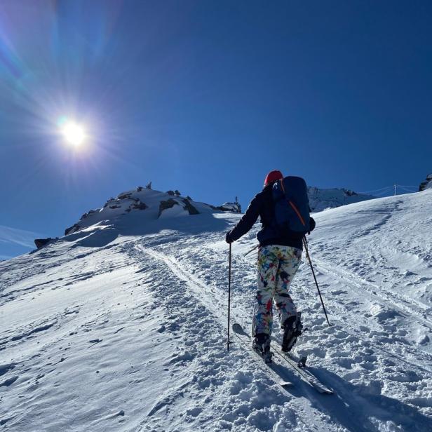 Eine Person steigt mit Skiern und Rucksack einen verschneiten Hang hinauf.
