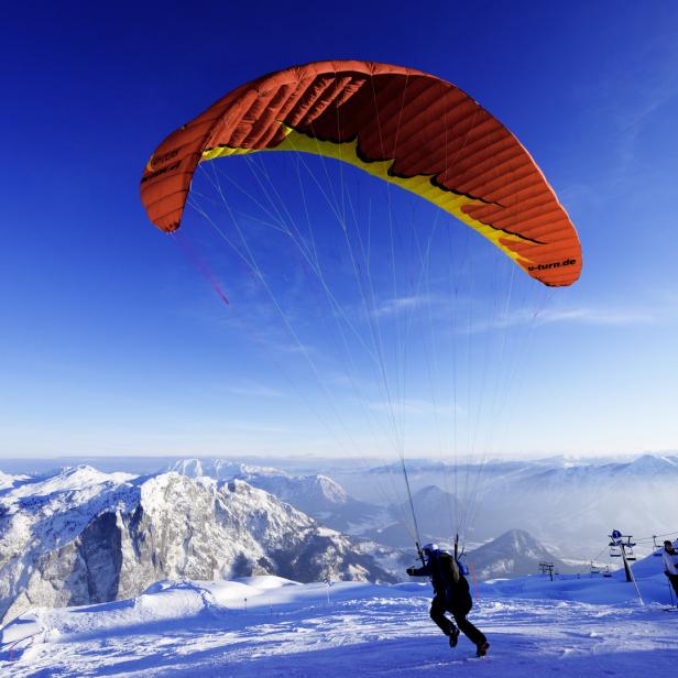 Ein Gleitschirmflieger startet auf einem schneebedeckten Berg mit Blick auf eine Berglandschaft.